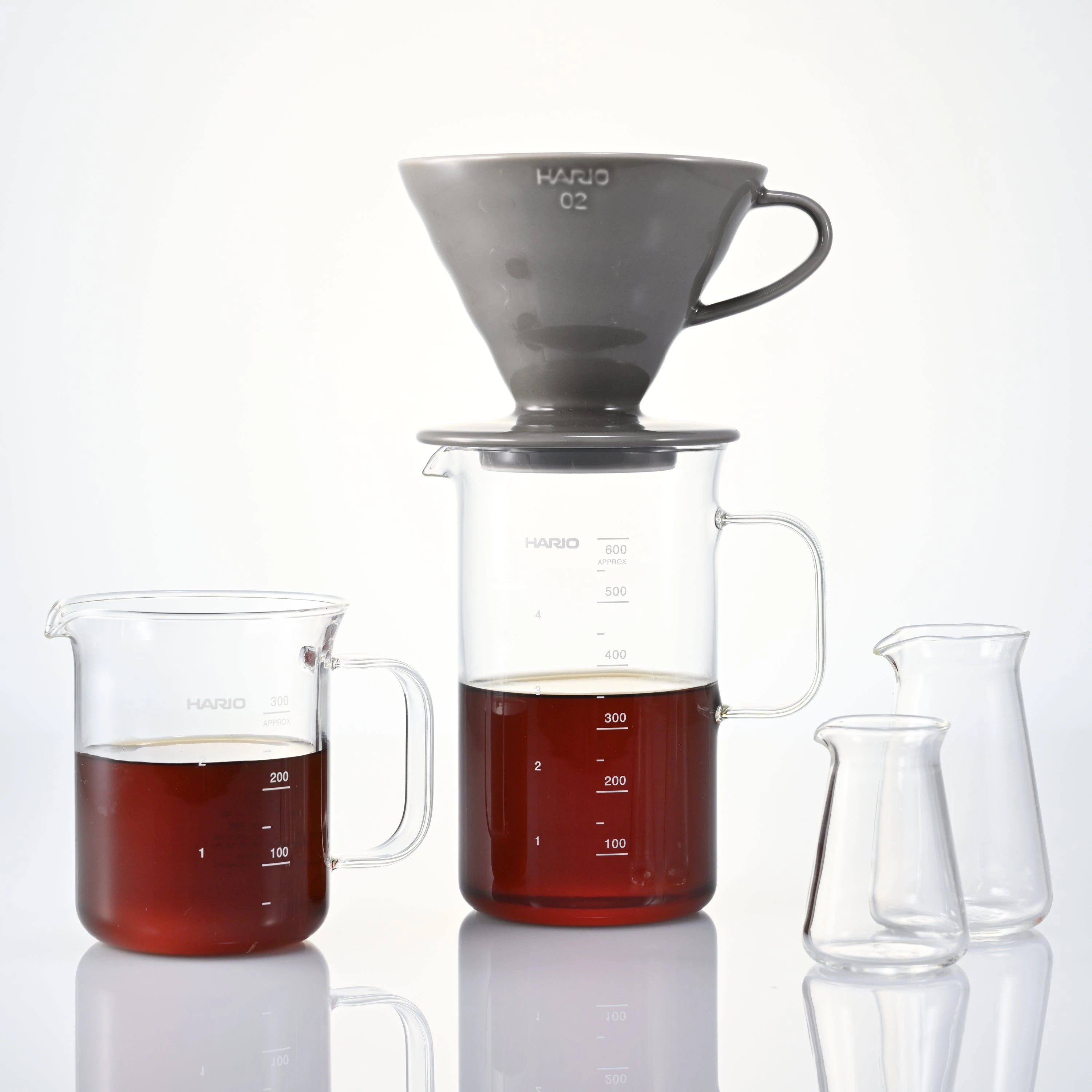 Hario glass brewing vessels and ceramic dripper arranged on white surface for pour-over coffee preparation