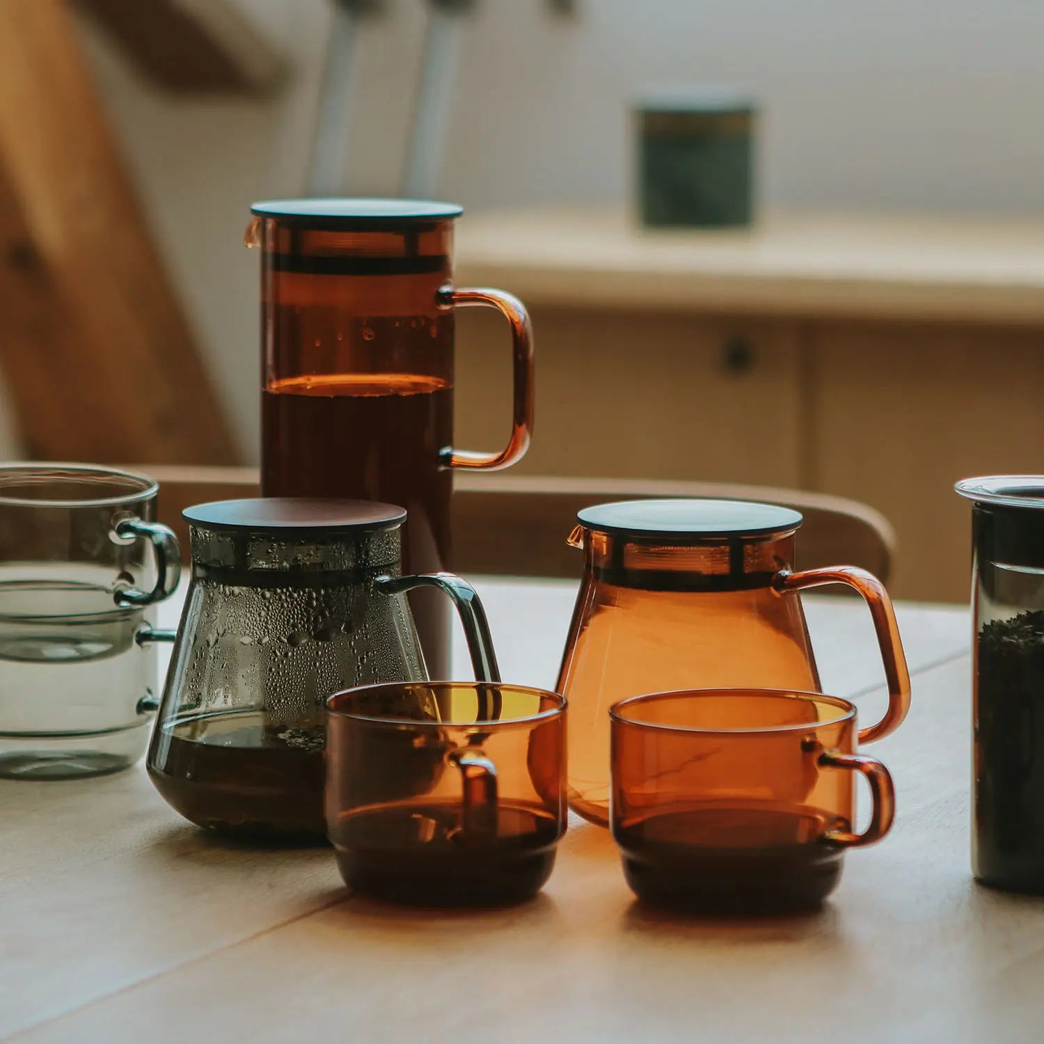 Assorted colored glass coffee and tea vessels including amber-toned mugs, pitchers, and brewing equipment arranged