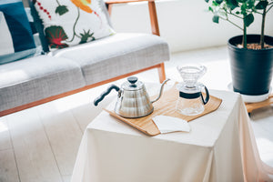 Hario V60 coffee brewing setup on wooden tray with kettle and dripper cone on living room table