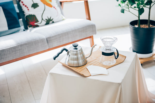 Hario V60 coffee brewing setup on wooden tray with kettle and dripper cone on living room table