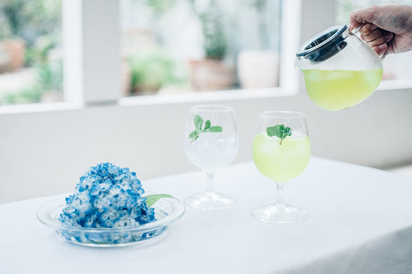 Brewed tea in Largo server with dripper resting on top beside white flowers and greenery.