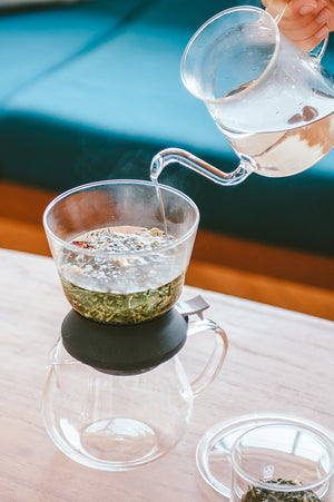 Pale green tea flowing from Largo dripper into clear serving cup with white background.