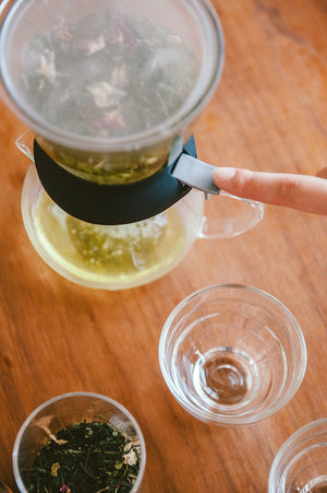 Hands carefully tilting Largo dripper mechanism to pour steeped tea into collection vessel.
