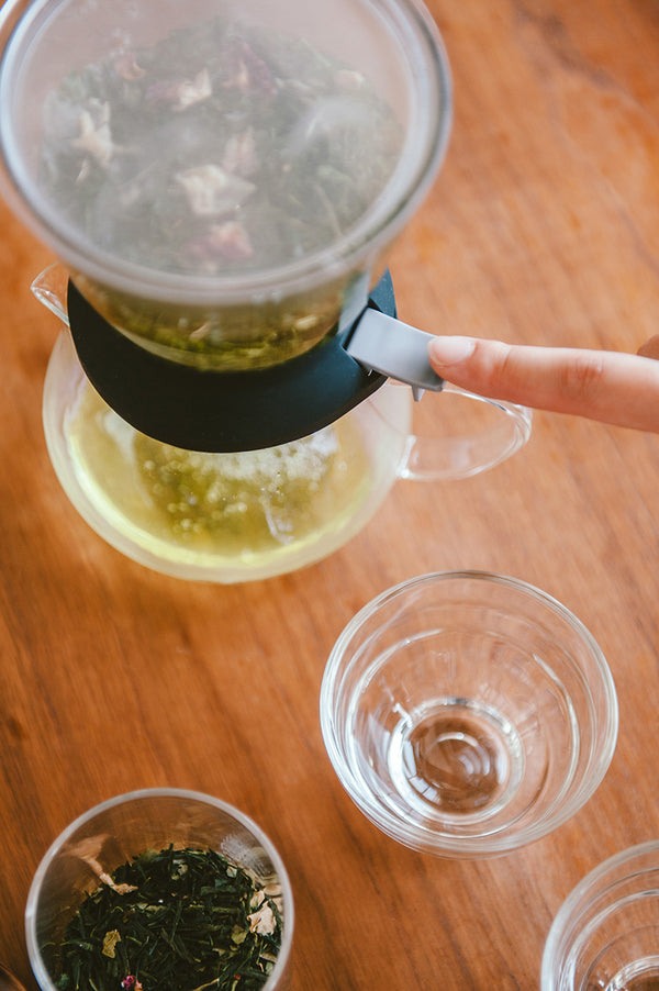 Hands carefully tilting Largo dripper mechanism to pour steeped tea into collection vessel.