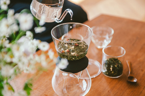 Water being poured into upper chamber of Largo dripper containing loose green tea leaves.