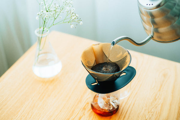 Hot water being poured into gold paper filter inside Hario V60 dripper positioned over glass carafe