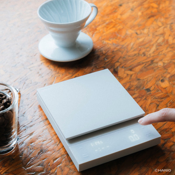 Hand touching white Polaris scale platform next to ceramic dripper and coffee beans