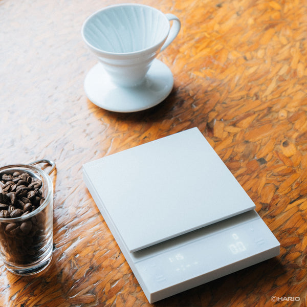 White ceramic pour-over coffee dripper and empty Polaris scale platform on wooden table