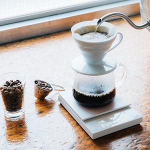 Hot water streaming into ceramic dripper on Polaris scale with coffee beans nearby