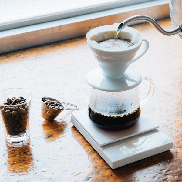 Hot water streaming into ceramic dripper on Polaris scale with coffee beans nearby