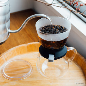 Two glasses of golden brewed tea beside filled Largo dripper on wooden serving tray.