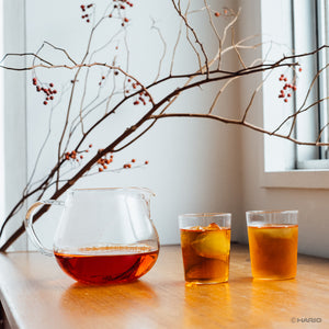 Wooden spoon placing green tea leaves into upper glass chamber of Largo dripper during setup.