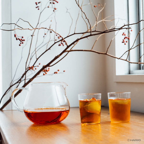 Wooden spoon placing green tea leaves into upper glass chamber of Largo dripper during setup.