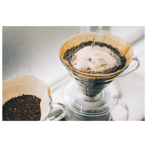 Water streaming through V60 coffee filter containing dark ground coffee.