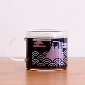 Glass mug filled with dark beverage, showing Mount Fuji illustration in purple and pink tones.