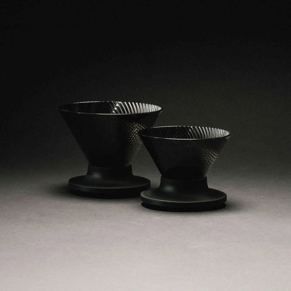 Two black ceramic V60 drippers with ridged interiors on pedestals, arranged side by side.