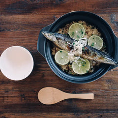Cooked mackerel fillet with lime slices and rice in a dark clay cooker on wooden surface