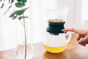 Person handling Largo tea dripper showing pale yellow brewed tea in server collection vessel.