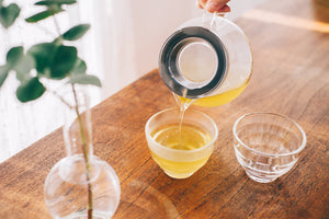 Close-up of pale yellow tea being poured from Largo dripper into small clear serving cup.