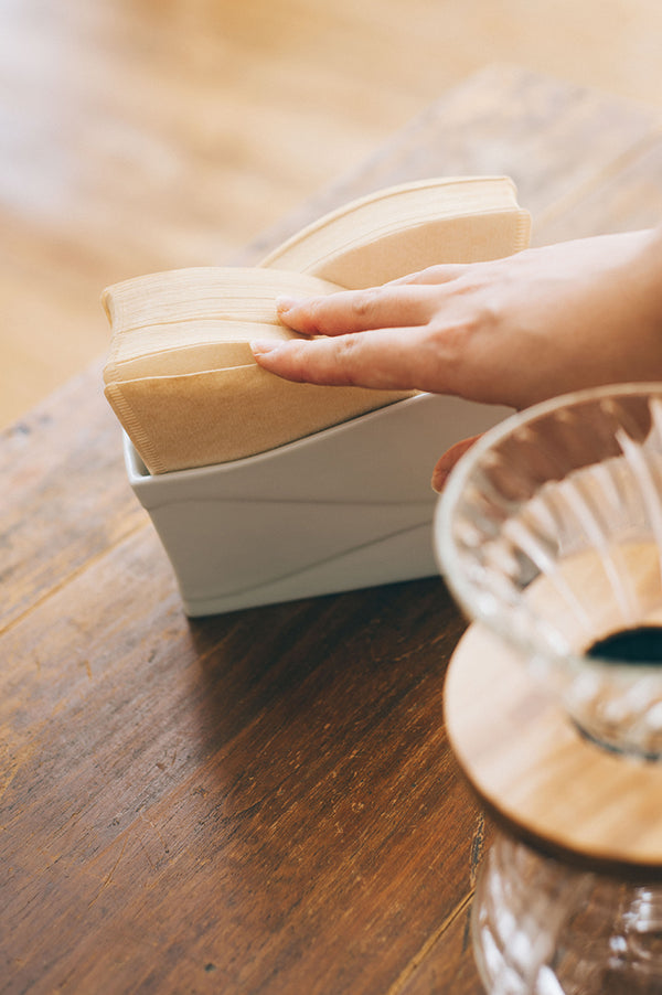 Close-up of hand removing folded coffee filter from white ceramic holder