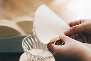 Hands positioning unfolded white V60 paper filter into glass dripper.