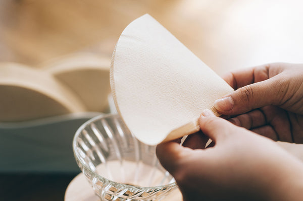 Hands positioning unfolded white V60 paper filter into glass dripper.
