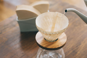 White V60 paper filter installed in glass dripper with metal drip stand.