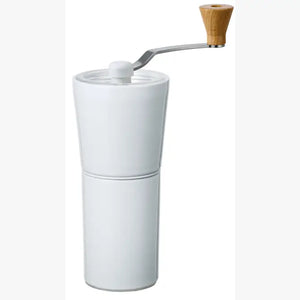 White ceramic coffee grinder with wooden knob crank handle against plain background.