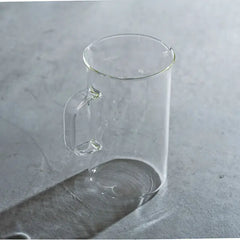 Clear glass beaker server with handle and measurement markings, displayed against gray marble surface.