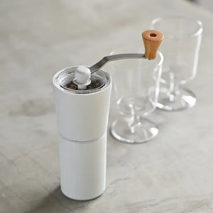White ceramic coffee grinder with wooden handle crank and glass burrs shown at angle.