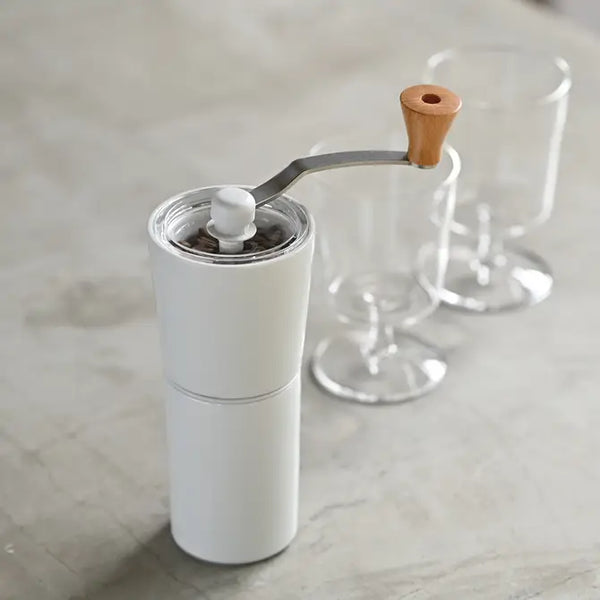 White ceramic coffee grinder with wooden handle crank and glass burrs shown at angle.