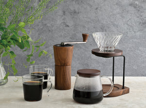 Complete walnut wood coffee brewing setup with grinder, glass cups, carafe, and pour-over cone.