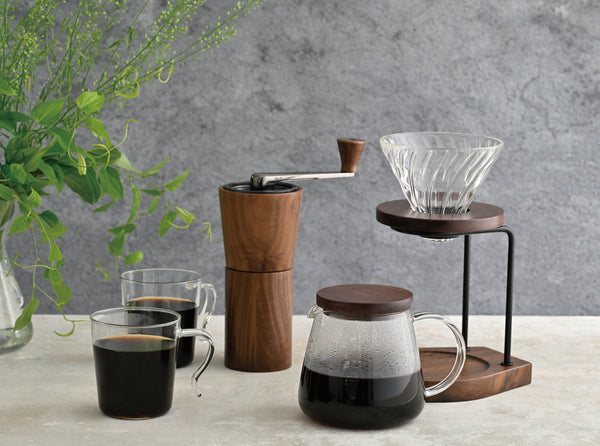 Complete walnut wood coffee brewing setup with grinder, glass cups, carafe, and pour-over cone.