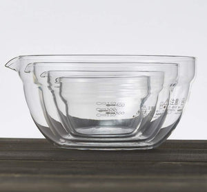 Four clear glass mixing bowls with spouts and measurement markings, nested together to show size progression from smallest