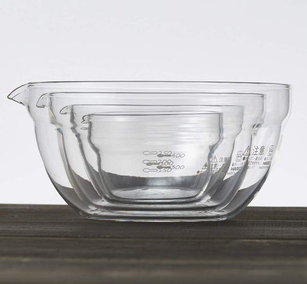 Four clear glass mixing bowls with spouts and measurement markings, nested together to show size progression from smallest