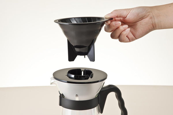 Hand holding removable black dripper basket with ribbed interior above glass carafe assembly.