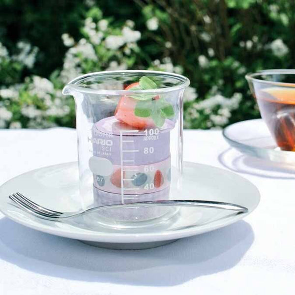 HARIO beaker with fruit and herbs displayed on white plate setting.
