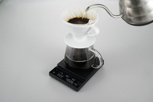 Black Polaris scale with ceramic dripper actively brewing coffee into collection glass