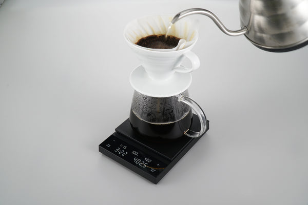 Black Polaris scale with ceramic dripper actively brewing coffee into collection glass