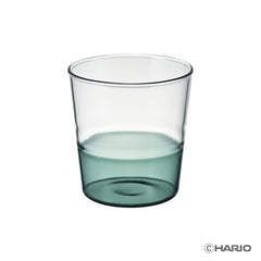 Clear HARIO drinking glass half-filled with teal-colored liquid against white background.