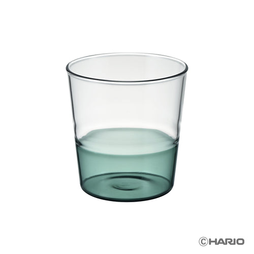 Clear HARIO drinking glass half-filled with teal-colored liquid against white background.