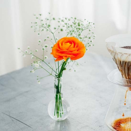 Bright orange rose with airy white baby's breath in teardrop vase on marble table.