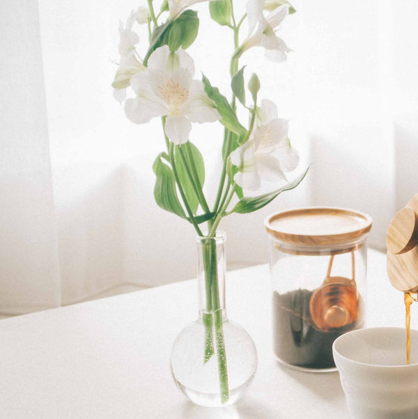 White jasmine flowers with green buds in glass vase beside wooden bowl and cup.