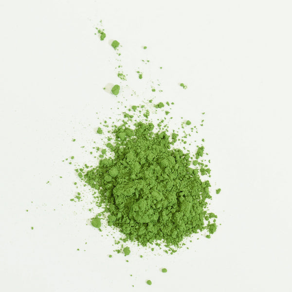 Loose matcha powder scattered on white surface showing fine, vibrant green texture.