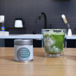 Finished matcha beverage in tall glass with ice next to product tin.