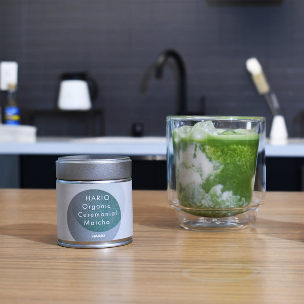 Finished matcha beverage in tall glass with ice next to product tin.
