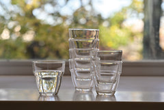 Multiple clear glass cups stacked in groups on windowsill with natural garden background.