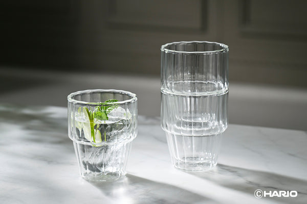 Two clear double-walled glasses with vertical ribbed pattern, one filled with water and fresh mint sprig on marble surface.