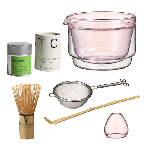 Matcha set with pink-tinted glass bowl and matching small pink glass cup, accompanied by green matcha powder containers