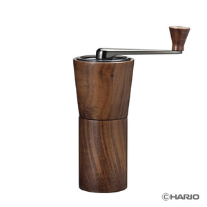 Walnut wood manual coffee grinder with black metal top and hand crank on white background.